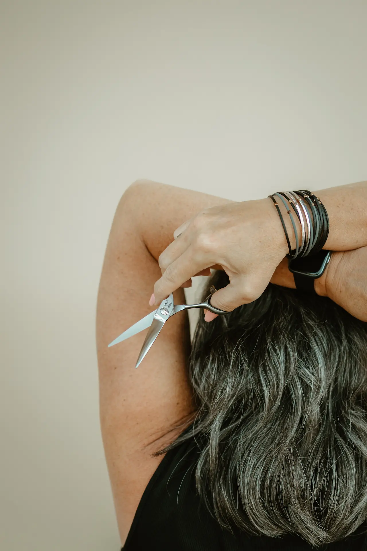 Diane Lichtas holds professional hair scissors while cutting gray hair, wearing silver bracelets on her wrist.